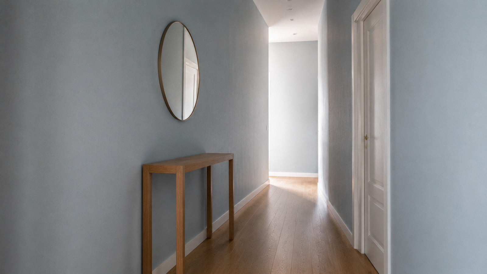 Corridoio domestico tinteggiato in azzurro con consolle in legno chiaro e specchio rotondo